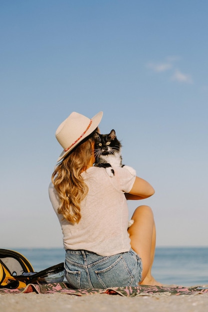 海の近くのビーチで猫と猫を抱く若い女性。ペットと一緒に旅行のコンセプト。