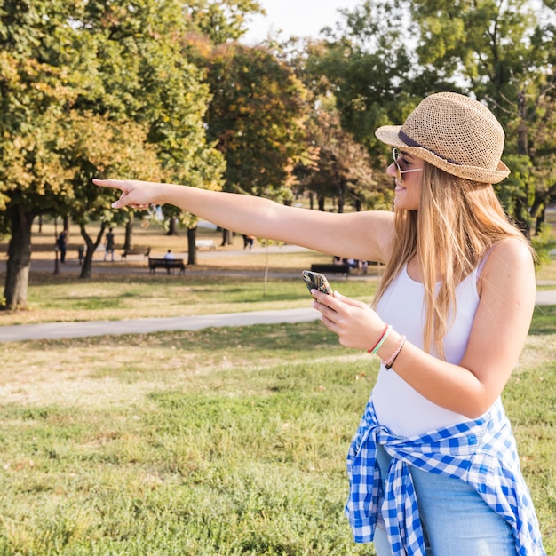 Бесплатное фото Молодая женщина с мобильного телефона, указывая на что-то