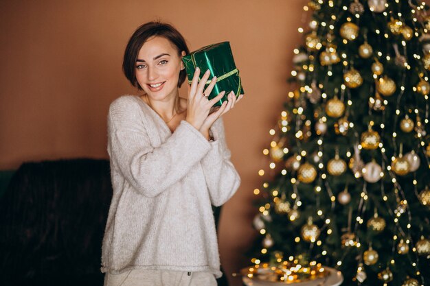 Young woman with Christmas present by the Christmas tree