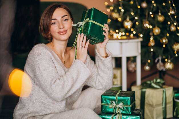 Young woman with Christmas present by the Christmas tree