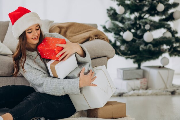 クリスマスツリーのそばでクリスマスプレゼントを持った若い女性