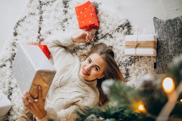 Молодая женщина с рождественскими подарками у елки
