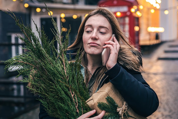 A young woman with a christmas tree and a gift box talking on the phone