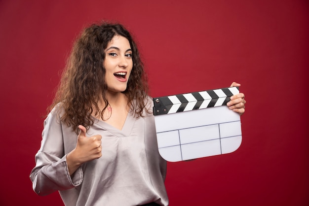 Young woman with clapperboard giving thumbs up.