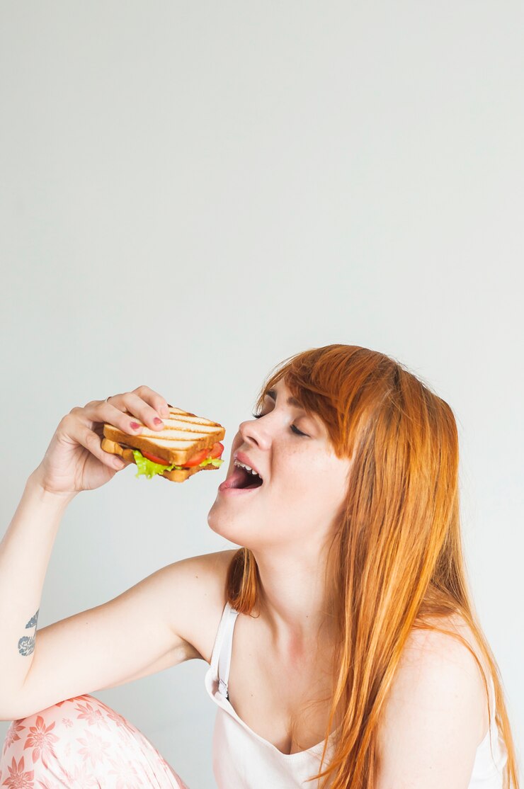 무료 Photo 닫힌 된 눈을 가진 젊은 여자는 흰색 배경에 구운 샌드위치를 먹고