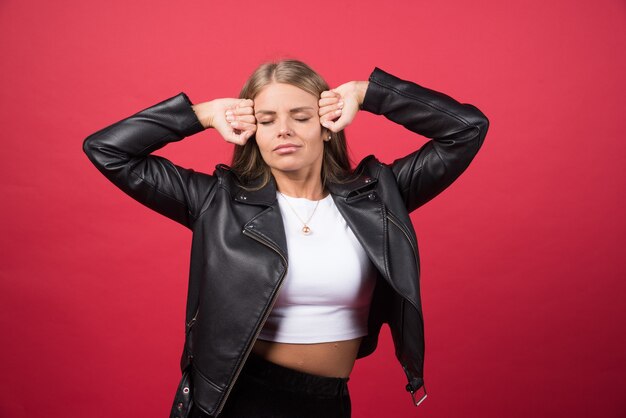 Young woman with closed eyes touching head against a red wall