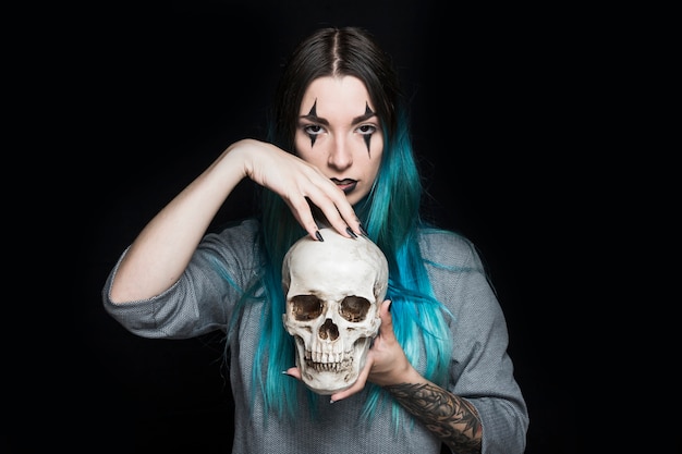 Free photo young woman with clown makeup standing with skull