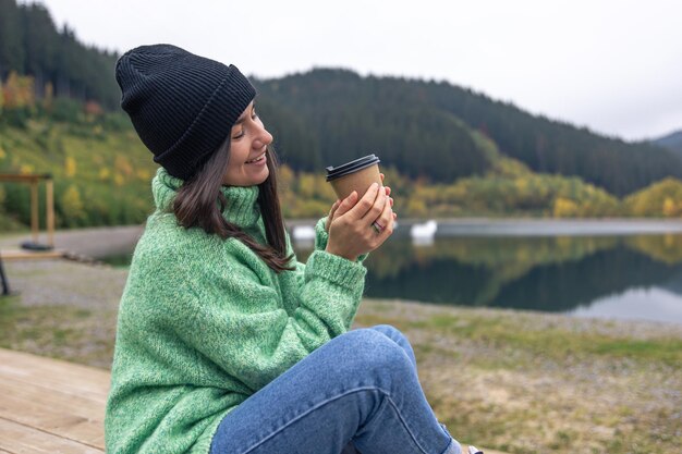 山のぼやけた背景にコーヒー カップを持つ若い女性