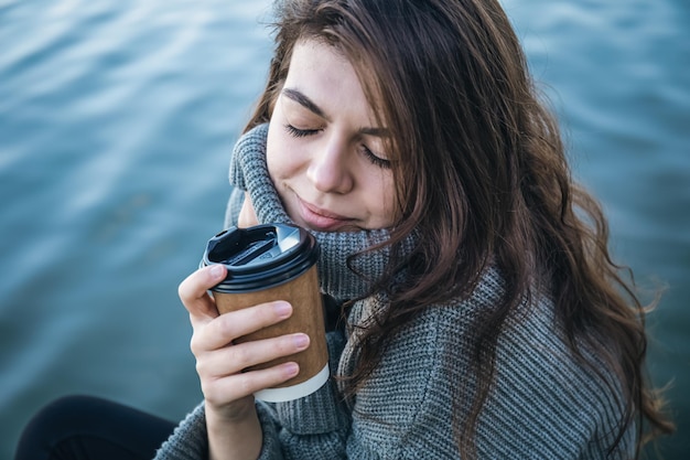 Una giovane donna con una tazza di caffè si siede vicino al fiume
