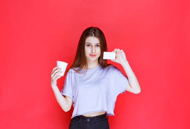 young woman with a cup of drink presenting her business card.