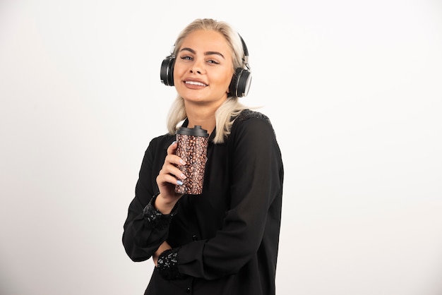 Young woman with cup in headphones on a red background. High quality photo