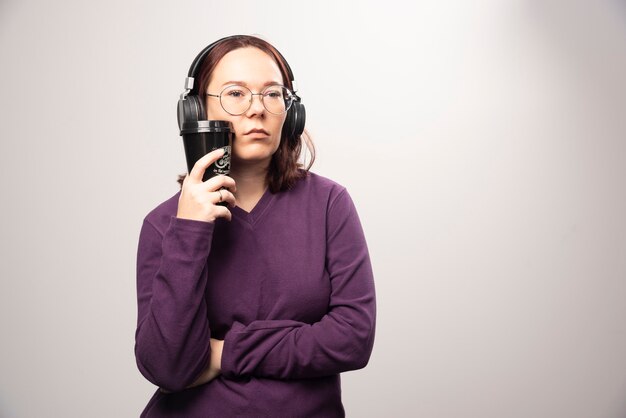 Young woman with cup posing in headphones on a white background. High quality photo