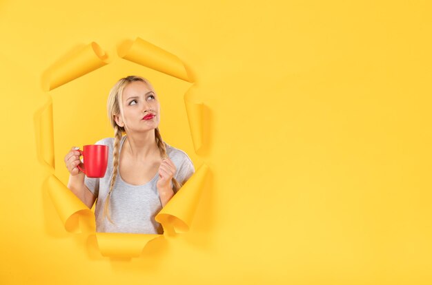 Young woman with cup of tea on torn yellow paper surface