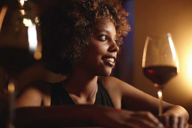 巻き毛と赤ワインのグラスを持つ若い女性