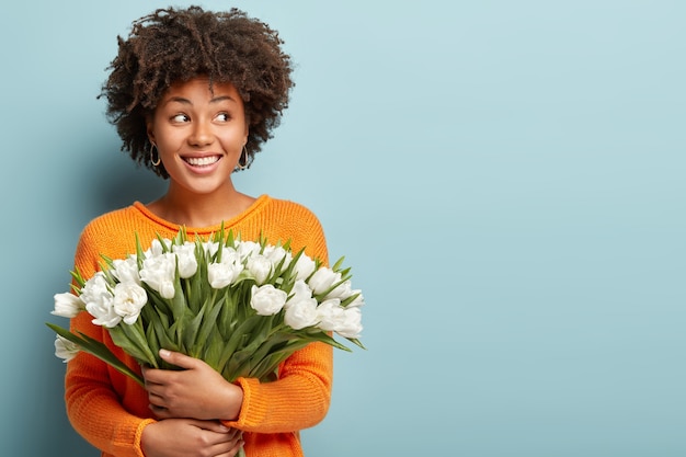 Foto gratuita giovane donna con capelli ricci che tiene il mazzo di fiori bianchi