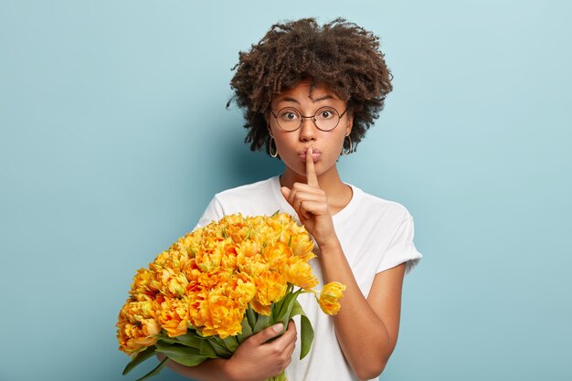 Young woman with curly hair holding bouquet of yellow flowers