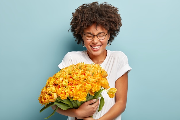 Young woman with curly hair holding bouquet of yellow flowers