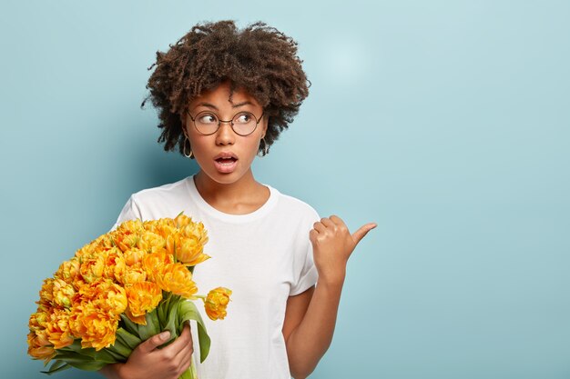 Young woman with curly hair holding bouquet of yellow flowers