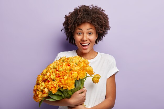 Young woman with curly hair holding bouquet of yellow flowers