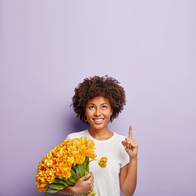 Young woman with curly hair holding bouquet of yellow flowers