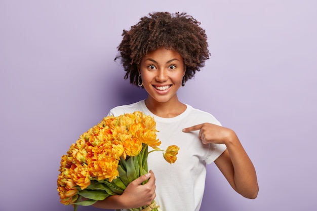 黄色い花の花束を保持している巻き毛の若い女性
