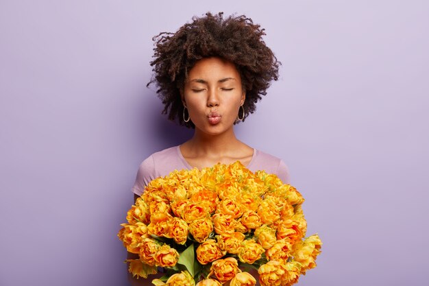 Young woman with curly hair holding bouquet of yellow flowers