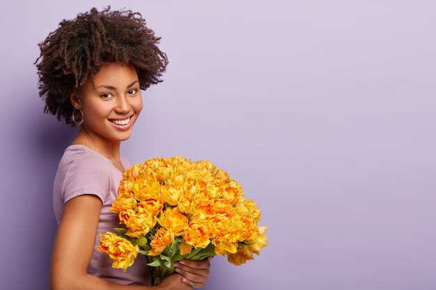 Young woman with curly hair holding bouquet of yellow flowers