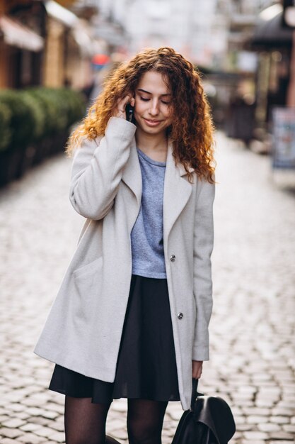 通りで電話を使用して巻き毛を持つ若い女性