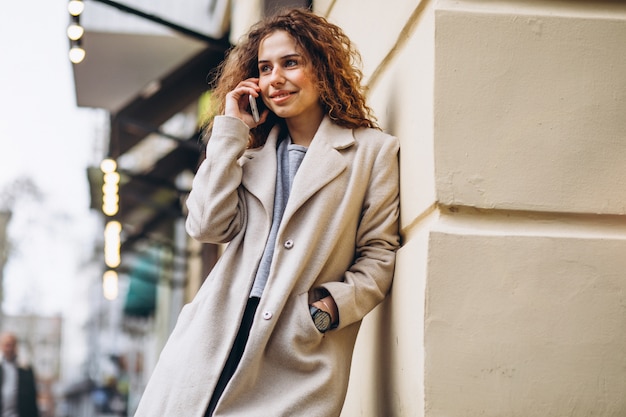 Free photo young woman with curly hair using phone at the street