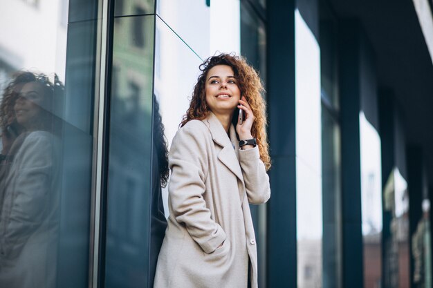 通りで電話を使用して巻き毛を持つ若い女性