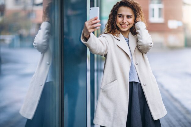 通りで電話を使用して巻き毛を持つ若い女性