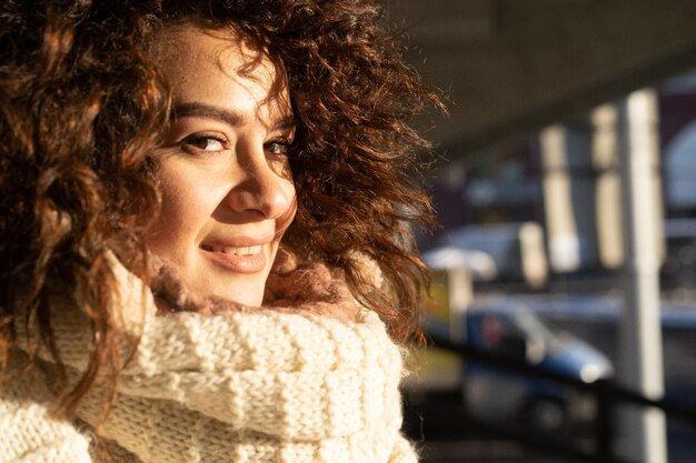 Young woman with dark curly hair, close-up portrait, warmly dressed scarf, winter frost, sunny day on the street in the city.