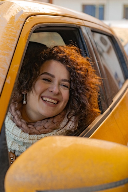 Free photo a young woman with dark curly hair driving a yellow car came to pick up takeaway food.