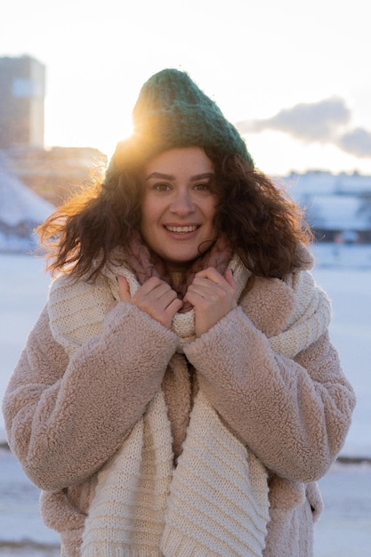 Young woman with dark curly hair in a winter hat, warmly dressed, winter frost, sunny day outside.