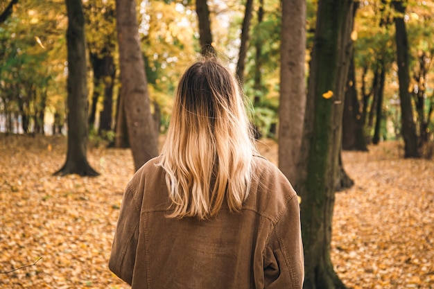 Free photo a young woman with dyed hair in the autumn forest view from the back