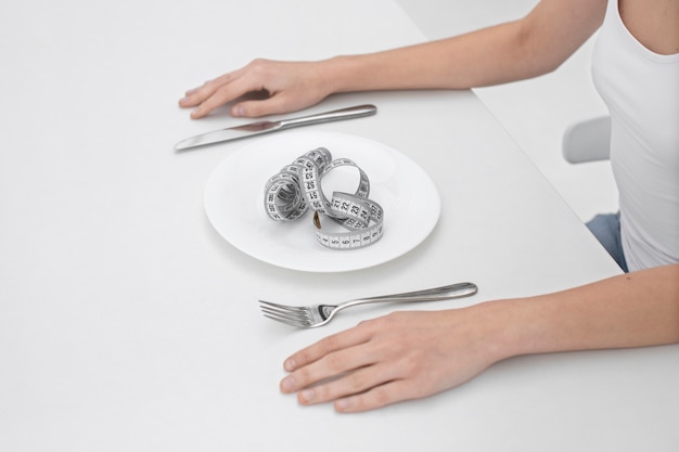Young woman with an eating disorder having a tape measure on the plate