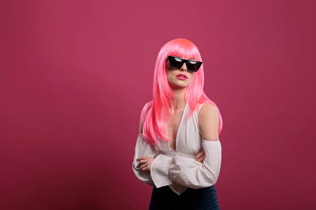 Young woman with elegant fashion style wearing trendy sunglasses, having confident and sexy attitude with pink hair. Feeling carefree and sensual with stylish modern eyewear in studio.