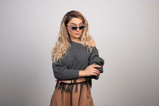 Young woman with eyeglasses standing on gray background. 