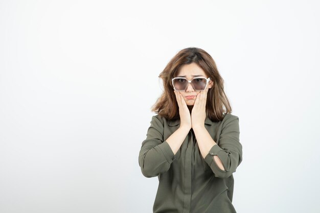 Young woman with eyeglasses standing and looking over white wall. High quality photo