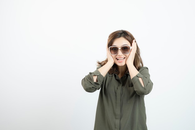 Young woman with eyeglasses standing and looking over white wall. High quality photo