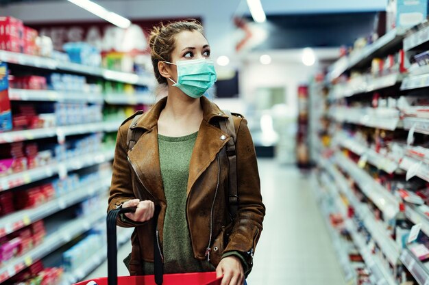 Молодая женщина в маске идет по продуктовому магазину во время пандемии COVID19