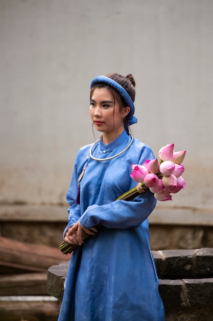 Foto gratuita giovane donna con bouquet di fiori che indossa un costume ao dai