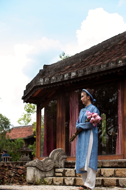 Foto gratuita giovane donna con bouquet di fiori che indossa un costume ao dai