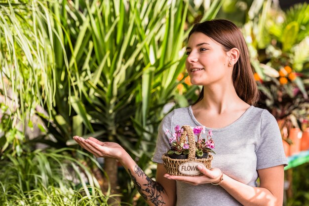 緑の植物で示すバスケットの花を持つ若い女