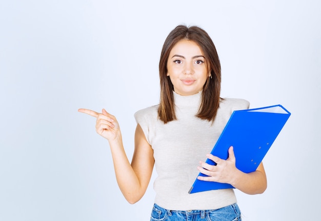 Young woman with a folder pointing away with an index finger.