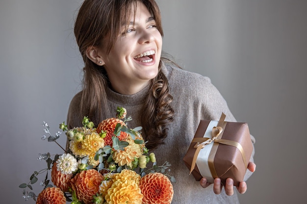 Giovane donna con una confezione regalo e un mazzo di fiori in mano