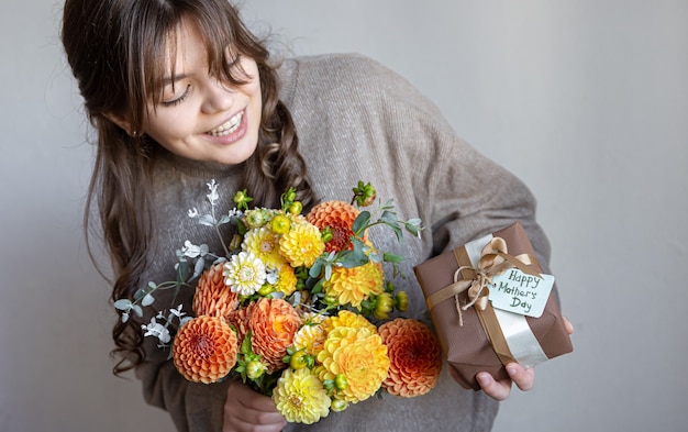 Young woman with a gift for mothers day and a bouquet of flowers in her hands