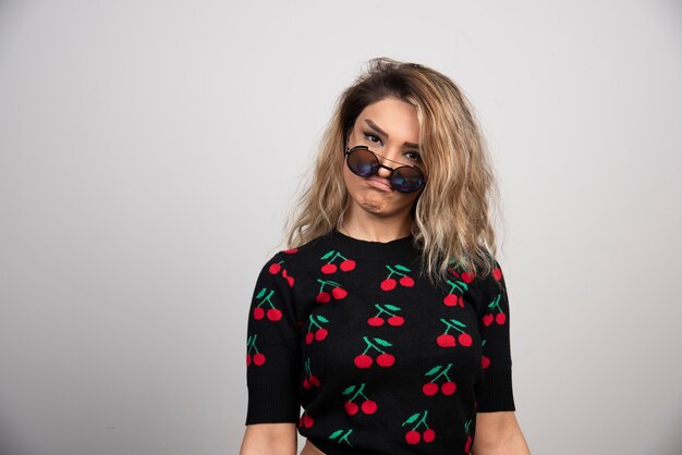 Young woman with glasses standing on gray wall. 