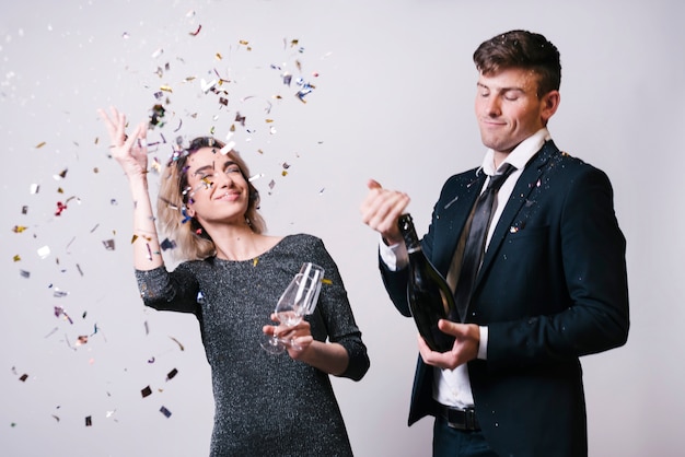 Free photo young woman with glasses tossing confetti near man with bottle of drink