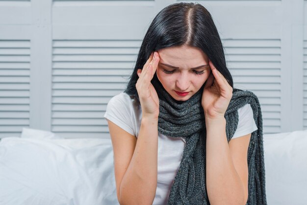 Young woman with gray scarf around her neck having headache touching her head